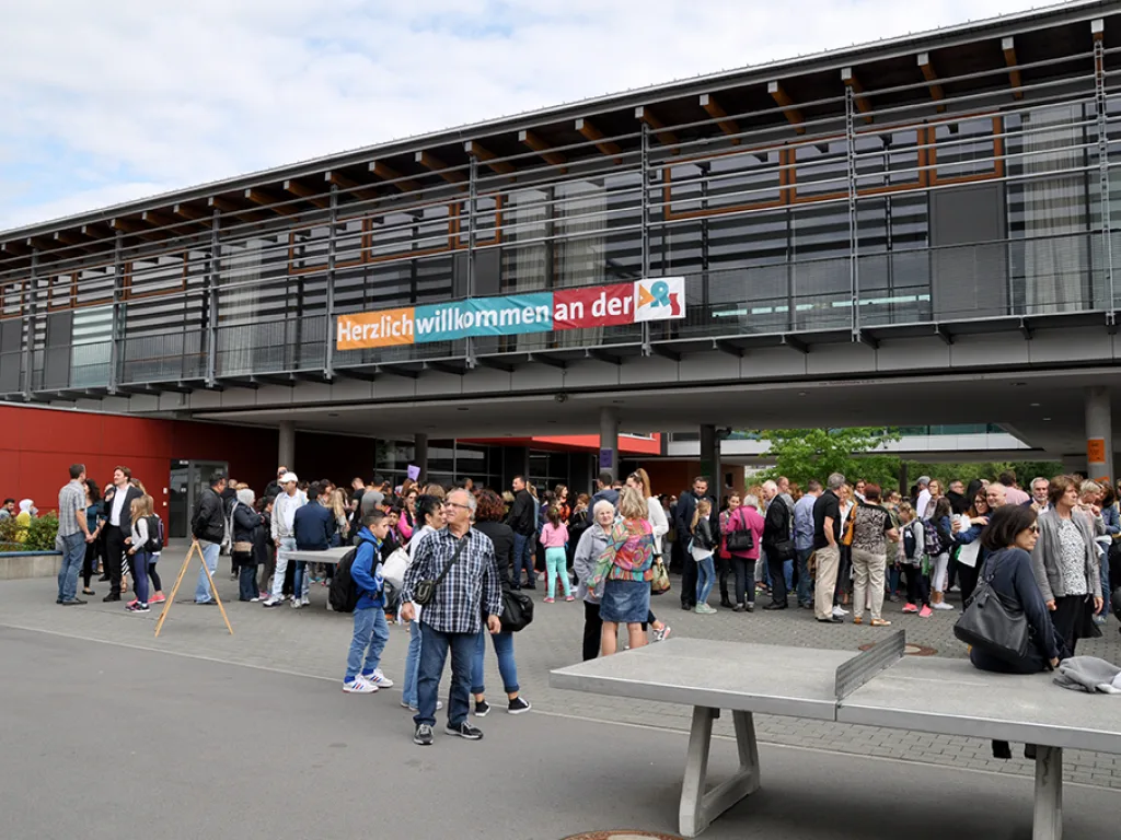 Gäste stehen auf dem Schulhof unter dem Willkommensbanner.